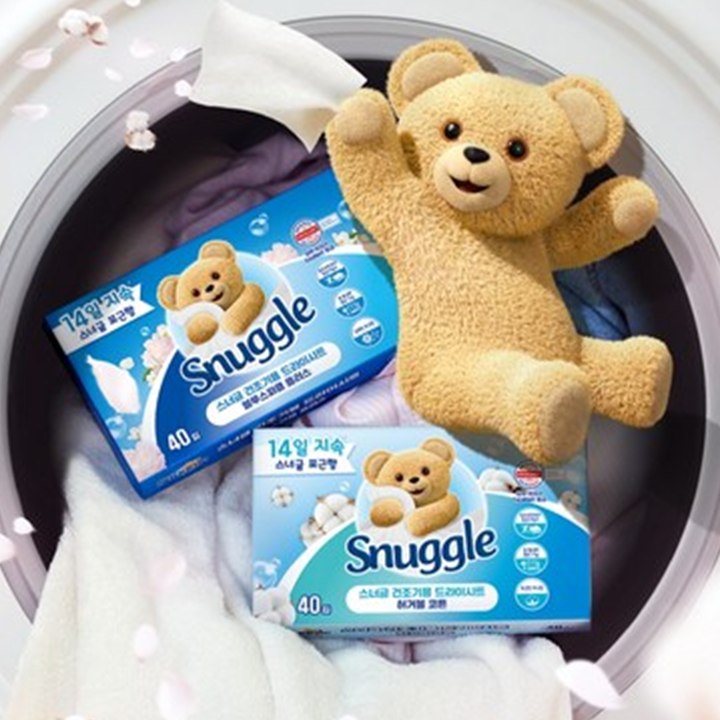 Snuggle dryer sheets in boxes with the brand's teddy bear, beside laundry in a drum